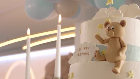 tiered baptism cake with teddy bear topper fondant and burning candles beside it
