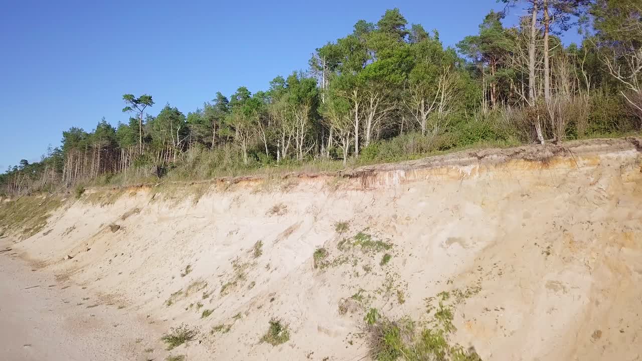 vista aérea de la playa del mar báltico en jurkalne en un día soleado, acantilado de arena blanca dañado por las olas, erosión costera, cambios climáticos, disparo de drones ascendentes de gran angular que avanza