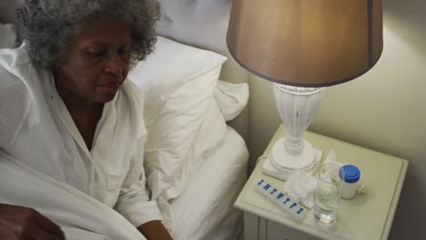 Kranke-ältere-Afroamerikanische-Frau-Trinkt-Wasser-Und-Liegt-Zu-Hause-Auf-Dem-Bett
