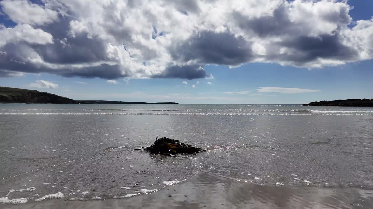 모래는 대서양의 부드러운 파도와 함께 파란 하늘에 낮은 푸프 구름을 반영합니다.