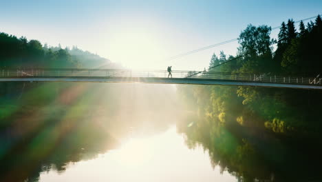 solo backpacker crosses bridge on sunny morning, tracking drone shot
