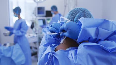 African-american-female-surgeon-wearing-surgical-cap,-putting-face-mask-on-in-operating-theatre