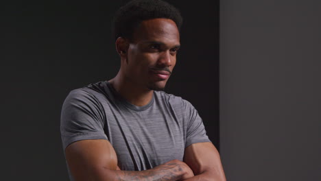 Studio-Portrait-Of-Smiling-Male-Athlete-Sport-Training-Or-Exercise-In-Gym-Folding-Arms-Against-Black-Background