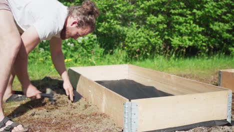 gardener setting-up wooden box for garden raised bed during sunny day