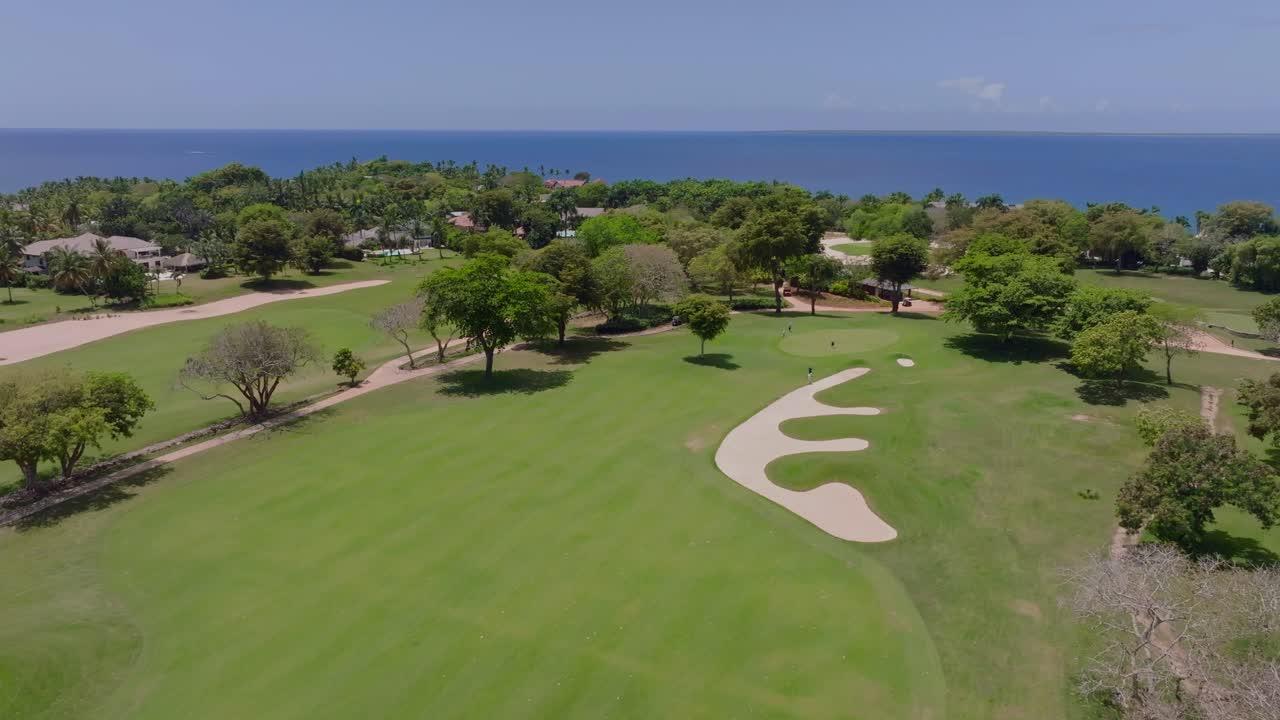 Vista aerea con drone di un campo da golf costiero a Casa de Campo, La Romana, Repubblica Dominicana, con giocatori di golf sul green, sfondo oceanico, palme e fairway curati vicino alla costa caraibica.