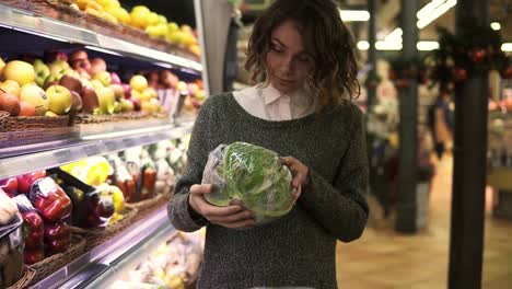 Mujer-Joven-En-Un-Supermercado-Moderno-Eligiendo-Repollo-Grande-En-El-Departamento-De-Vegetales-Orgánicos-Y-Poniéndolo-En-Un-Carrito.-Mujer-Sana