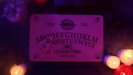 close up video of a wooden ouija board on a table surrounded by candles and a cross in a muffed - close up video of a wooden ouija board on a table. wax candles and a cross around. the planchette is slowly moving across the board, spelling out words and numbers. creative mystical content