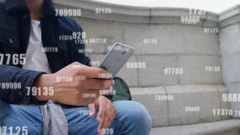 Animation-of-falling-changing-numbers-over-biracial-man-scrolling-on-smartphone-in-outdoors