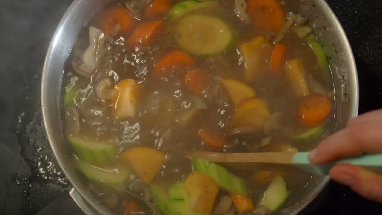 vista de arriba hacia abajo de una sopa de verduras que se agita en una olla humeante en cámara lenta 4k