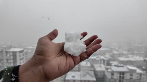 bola de nieve en la mano con vista del paisaje urbano nevado