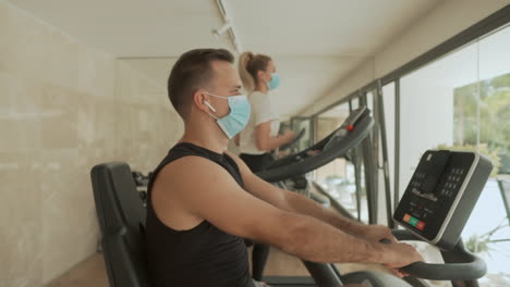 athlete male and female with face mask using exercise machines in the gym