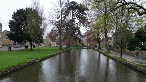 Low-drone-along-river-Windrush-Bourton-on-the-Water-Cotswold-village-UK