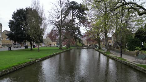 Niedrige-Drohne-Entlang-Des-Flusses-Windrush-Bourton-Auf-Dem-Wasser-Cotswold-Village-UK