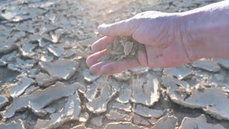 man holding some sand in the hand on cracked ground soil