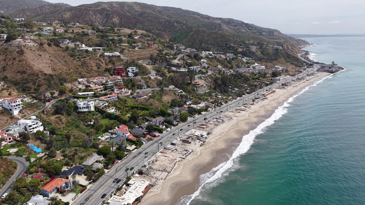 Filmato aereo cinematografico diurno ripreso da drone, catturato da un'angolazione lungo la costa della California, che mostra l'iconica Pacific Coast Highway che corre parallela al litorale
