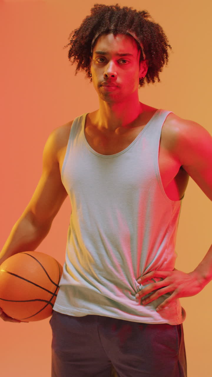 video vertical de un jugador de baloncesto masculino biracial con una pelota en un fondo naranja