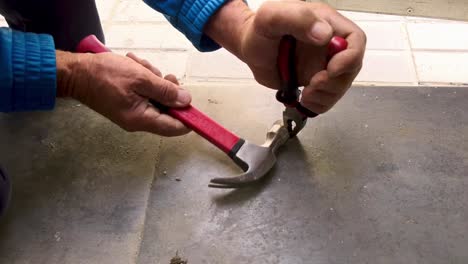 person is using hammer at job site, with linesman pliers holding tight metal screw in order to pull it out