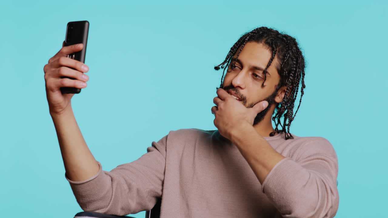 Man in wheelchair saluting friend over online videocall on cellphone, studio