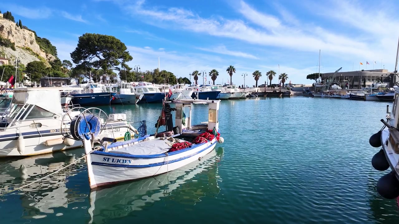 Tradizionali barche da pesca bianche riposano su calme acque turchesi nel pittoresco porto di Cassis.