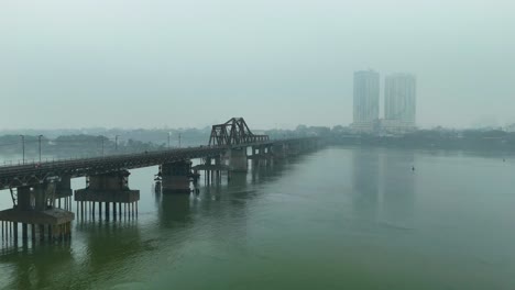 aerial: long bien bridge with fog and extreme pollution during the day in hanoi, the capital city of vietnam, push in drone shot