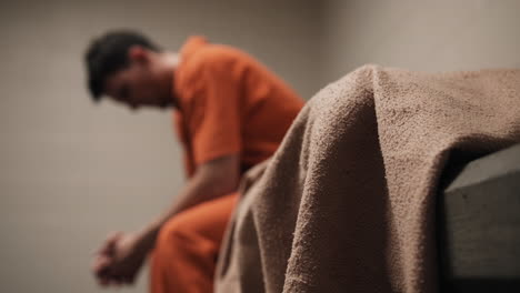 Ein-Trauriger-Mann,-Verurteilter-Krimineller,-Gefängnisinsasse-In-Orangefarbener-Uniform,-Der-Auf-Dem-Bett-Sitzt
