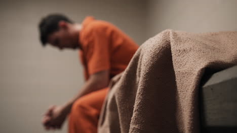 a sad man, convicted criminal, prison inmate in orange uniform sitting on bed