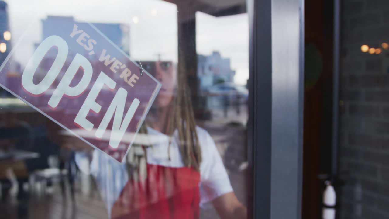 barista de raza mixta con dreadlocks cerrando la puerta y cambiando el cartel de abierto a cerrado