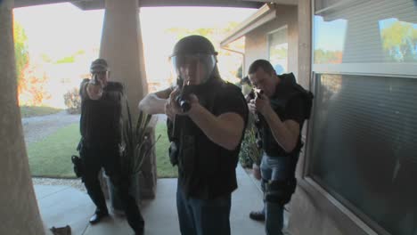 dea or swat officers with arms drawn perform a drug raid on a house 1