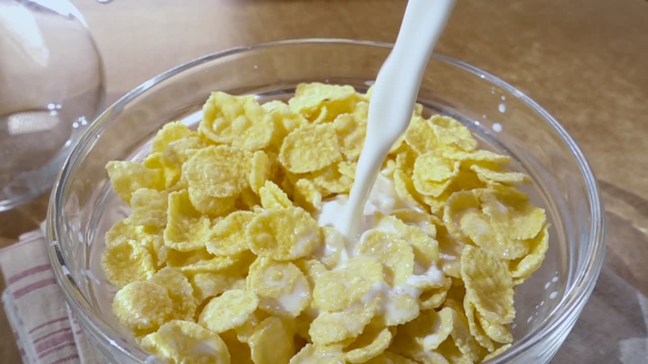 Knusprige gelbe Cornflakes in die Schale für ein köstliches Frühstück mit Milch am Morgen. Zeitlupe mit rotierender Kamerafahrt
