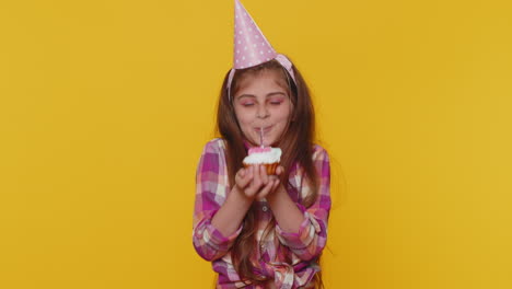 Happy-child-girl-kid-celebrating-birthday-party,-makes-wish-blowing-burning-candle-on-small-cupcake