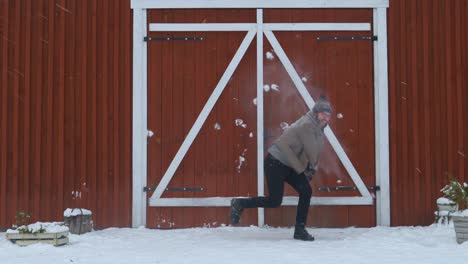 hipster playing with snowballs in front of a red wooden house in slow motion