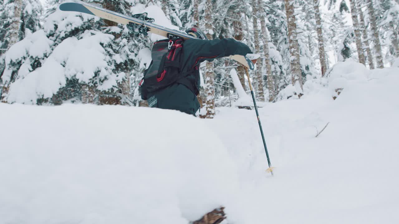 siguiente plano de un hombre caminando en la nieve profunda con esquís al hombro