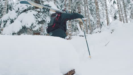 following shot of a man walking in deep snow carrying skis on shoulder