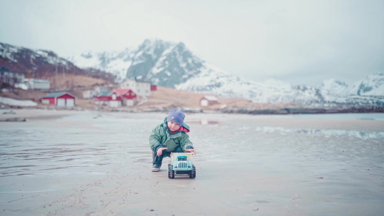 Dreng leger med legetøjslastbil på en smuk strand i Nordnorge lige uden for Tromsø, Norge. Med store bjerge i baggrunden er dette et fantastisk billede. #untraceableglobal