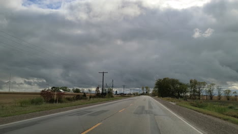 Speeding-down-a-country-road-before-a-storm-past-wheat-crops-and-farm-buildings