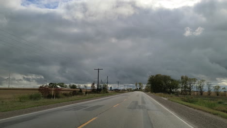 acelerando por una carretera rural antes de una tormenta pasando cultivos de trigo y edificios agrícolas