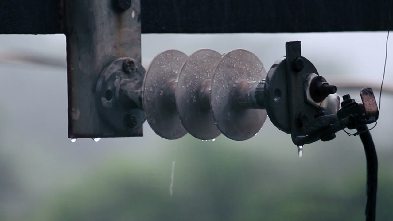 Close-up shot of rainwater dripping on electrical insulator during rainfall. Useful for energy, safety, weather, industry and infrastructure themes.