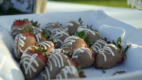 a plate of chocolate covered strawberries outside on a table in the summertime