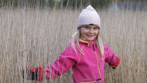 smiling little blond girl playing on meadow on winter day and looking in camera