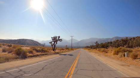 driving towards the mountains along a desert road with the sun high in the sky - point of view