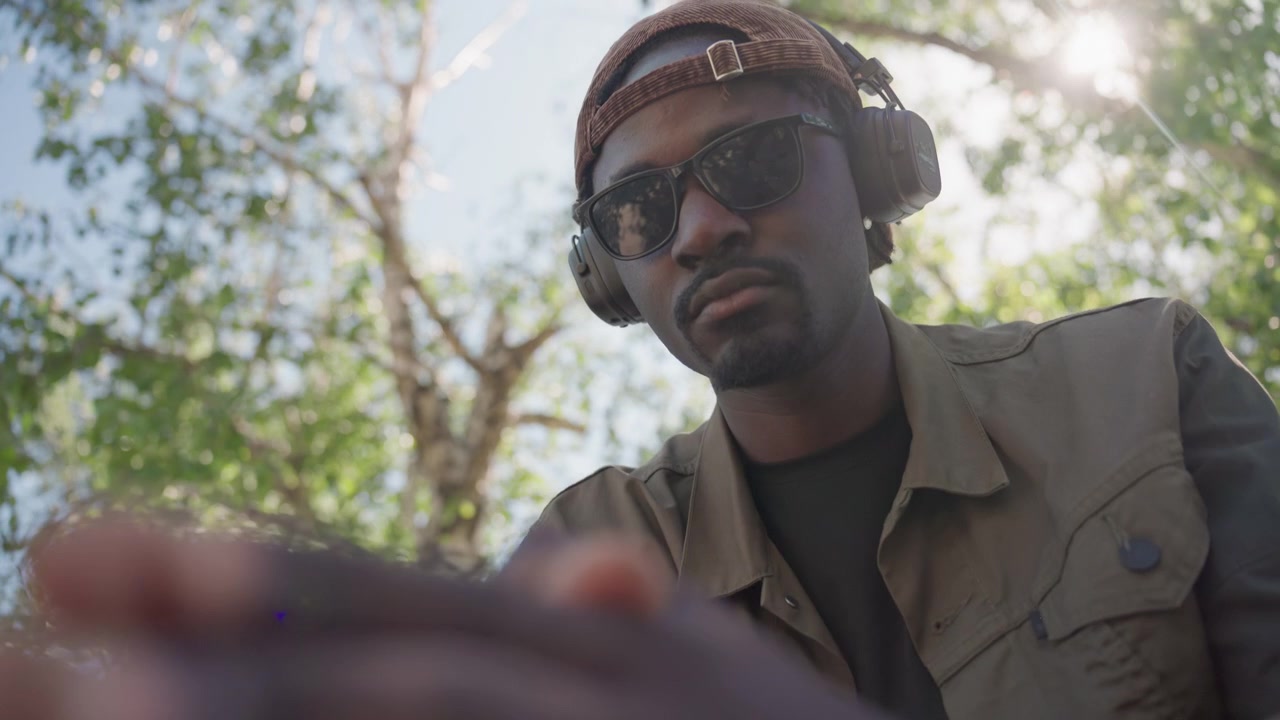 Close up of man wearing sunglasses and ear protection gesturing with his hands in outdoor setting. subject is dressed in military style clothing while interacting expressively