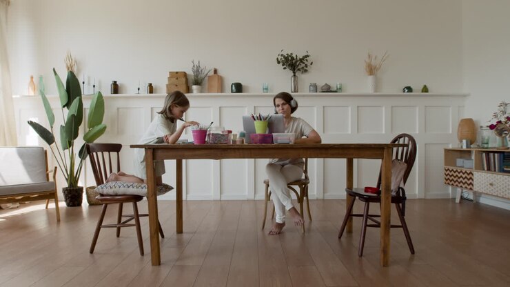 Wide Shot Of A Mother Making A Videocall While Her Daughter Is Seated Next To Her Doing Her Homework
