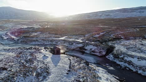 impresionante paisaje de casa solitaria en un campo nevado en islandia cerca de la corriente que fluye en un brillante día de invierno - toma aérea de drones