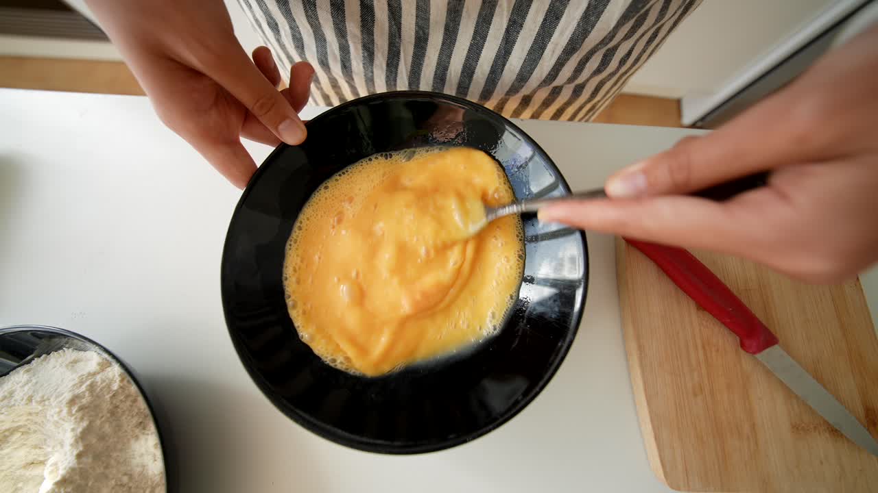 Close-Up of Hands Whisking Eggs in a Black Bowl