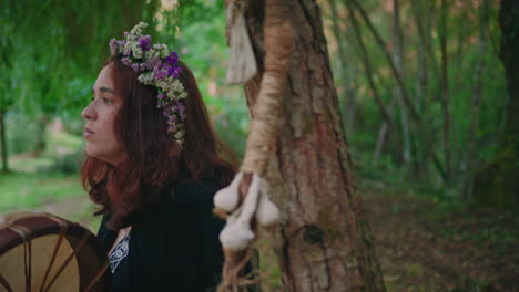 druid girl in a forest playing a shamanic drum side view close shot