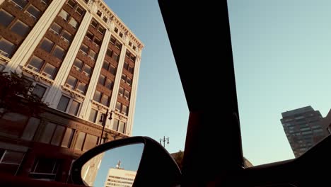pov shot from car driving under pedestrian bridge; reveals commercial buildings and bright blue sky at golden hour
