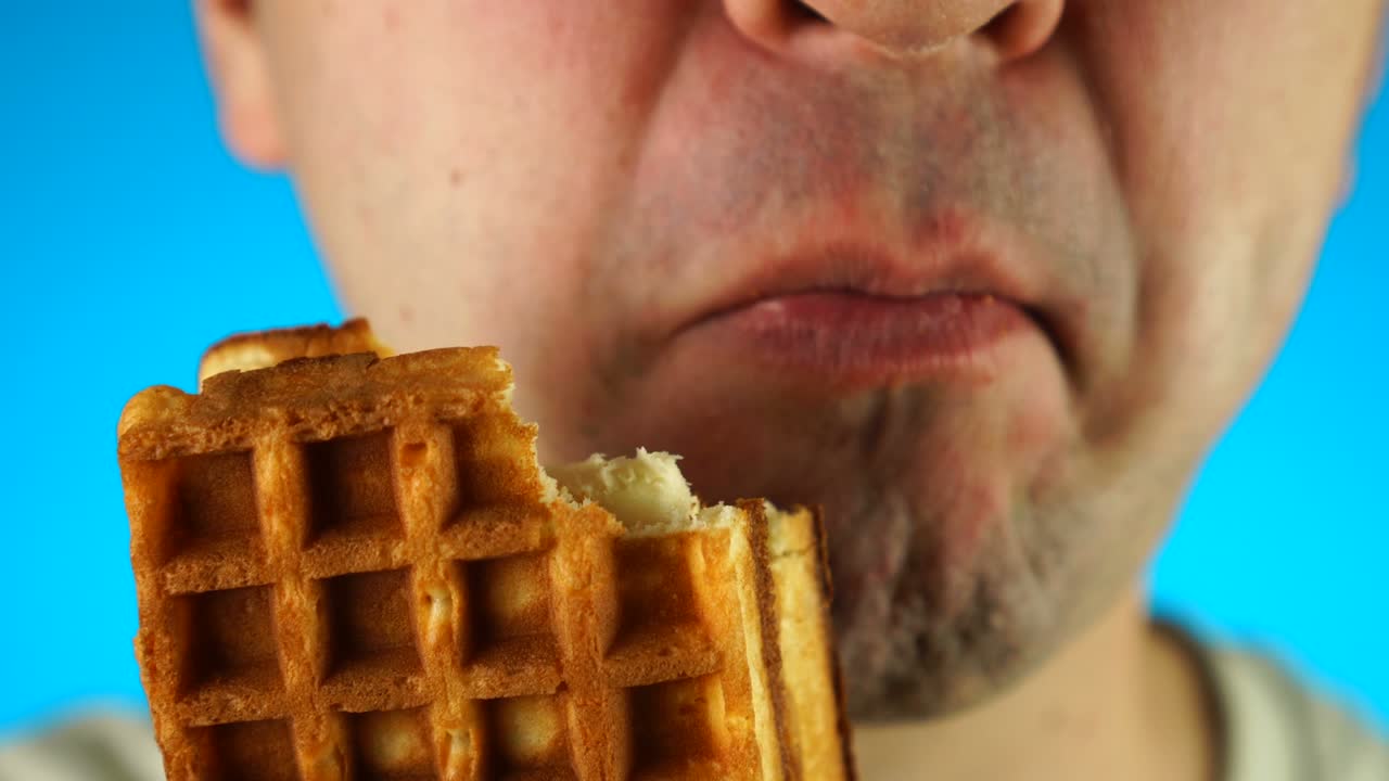 мужчина кусает и ест печенье или вафли. близко к нижней половине мужского лица, ест сладкую еду.