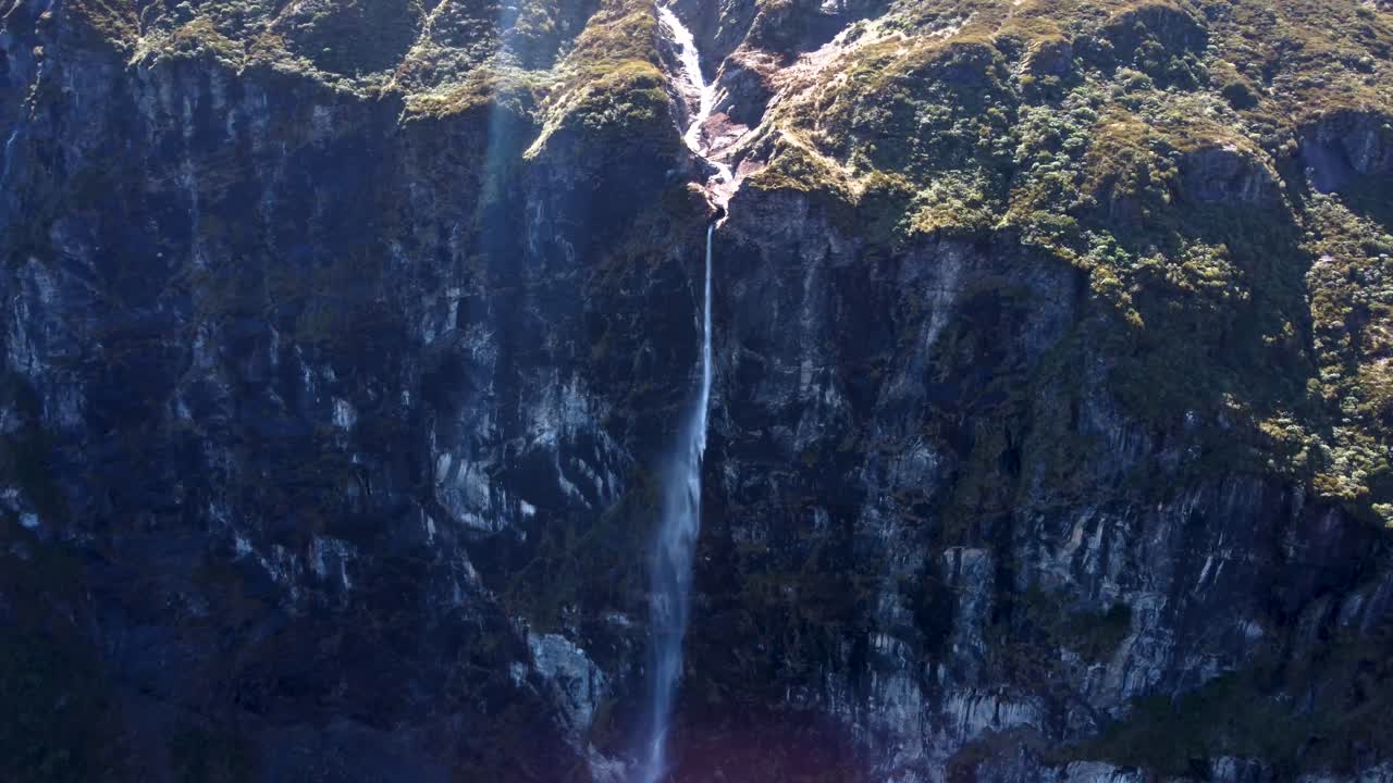 Drone view of a tall waterfall on a rock on a sunny day at Rob Roy Glacier, Wanaka, New Zealand.