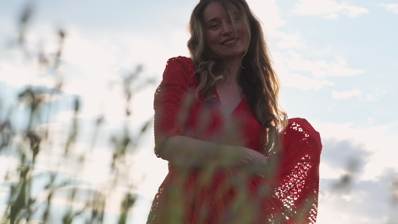 A carefree woman in a red lace dress dances among tall grass and wildflowers