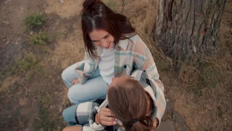 disparos de primer plano: dos amigas se balancean en un columpio de madera, hablando y arreglando el cabello de la otra. descanso en la casa de campo